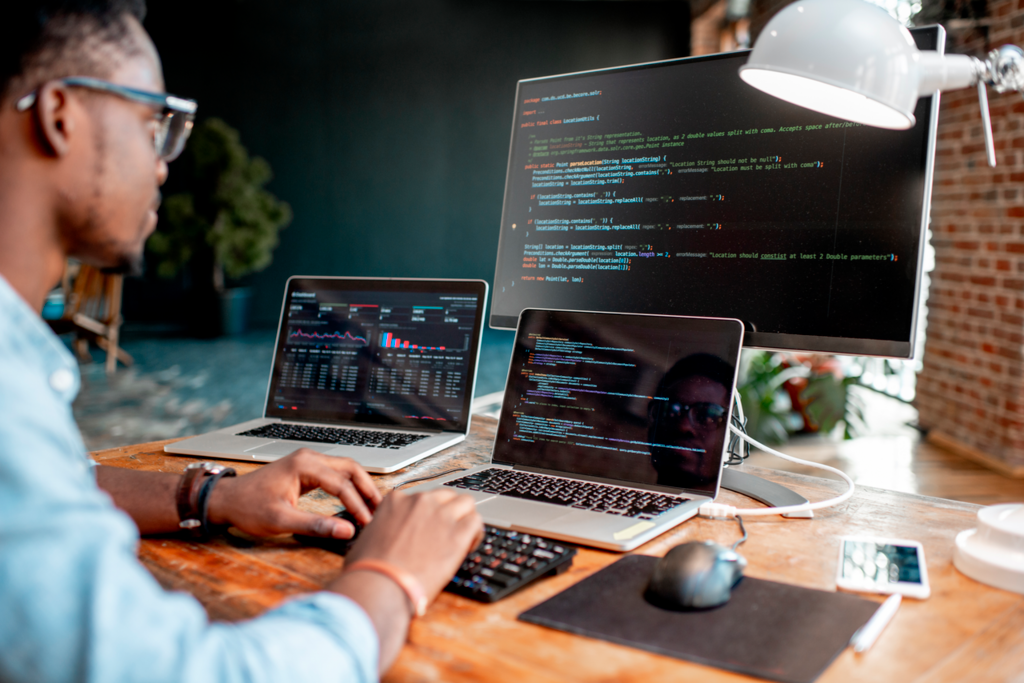 Momentum_Young_african_male_programmer_writing_program_code_sitting_at_the_workplace_with_three_monitors_in_the_office._Image_focused_on_the_screen-low-res.png